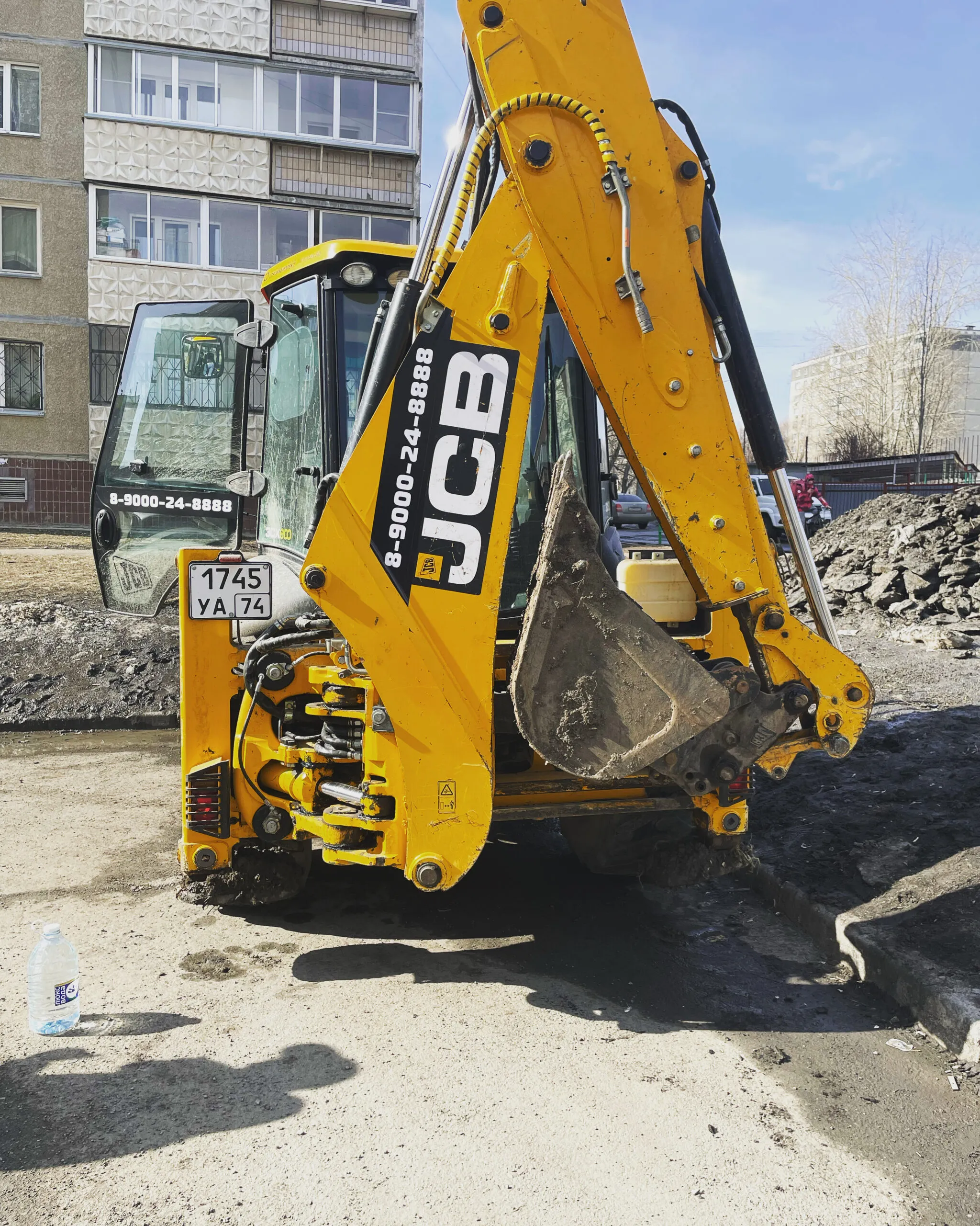 Экскаватор-погрузчик JCB на земляных работах во дворе жилого дома